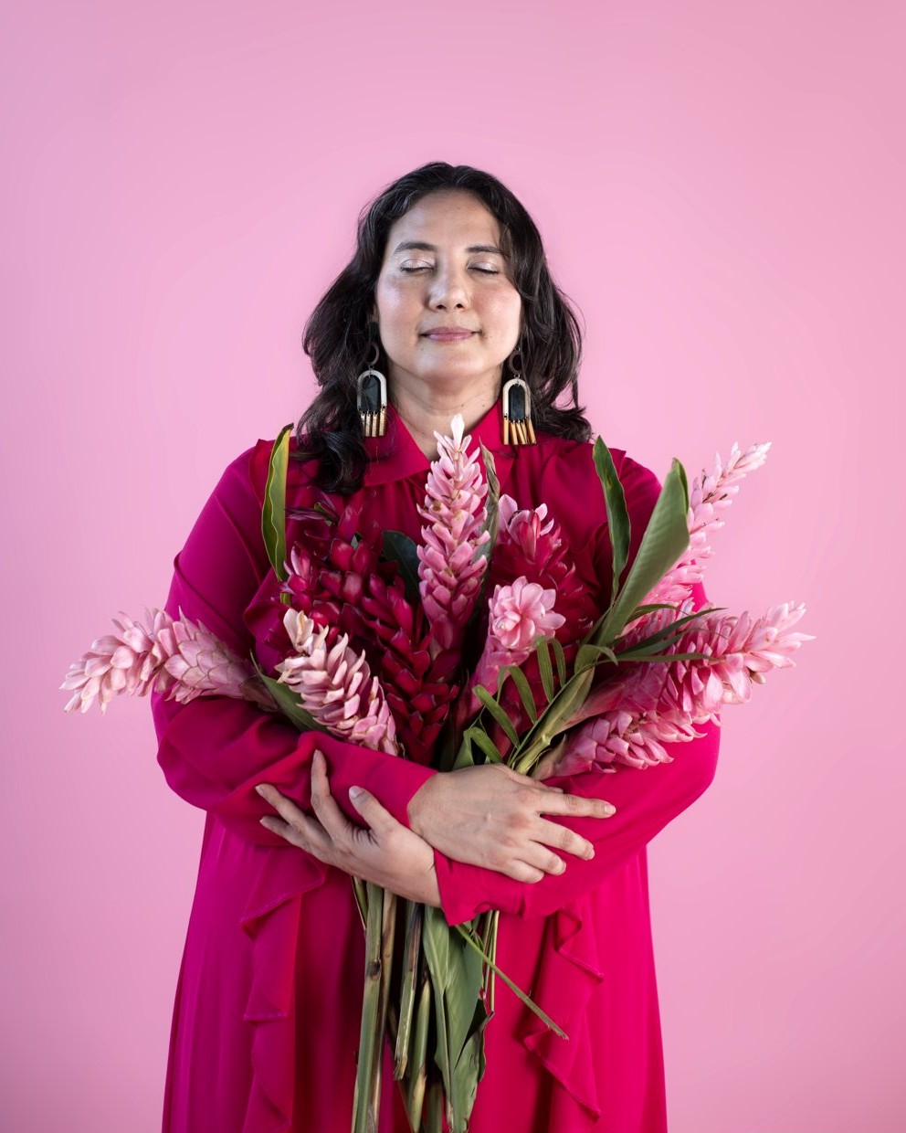 Alejandra Porta, eyes closed, hugging a bouquet of pink ginger flowers